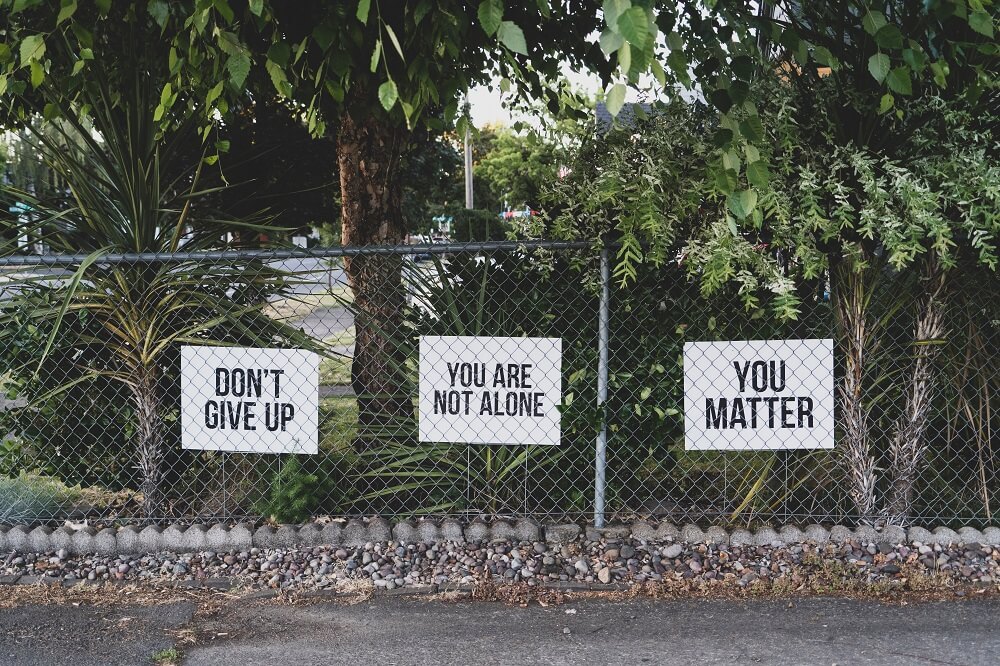 three affirming signs hang on a fence